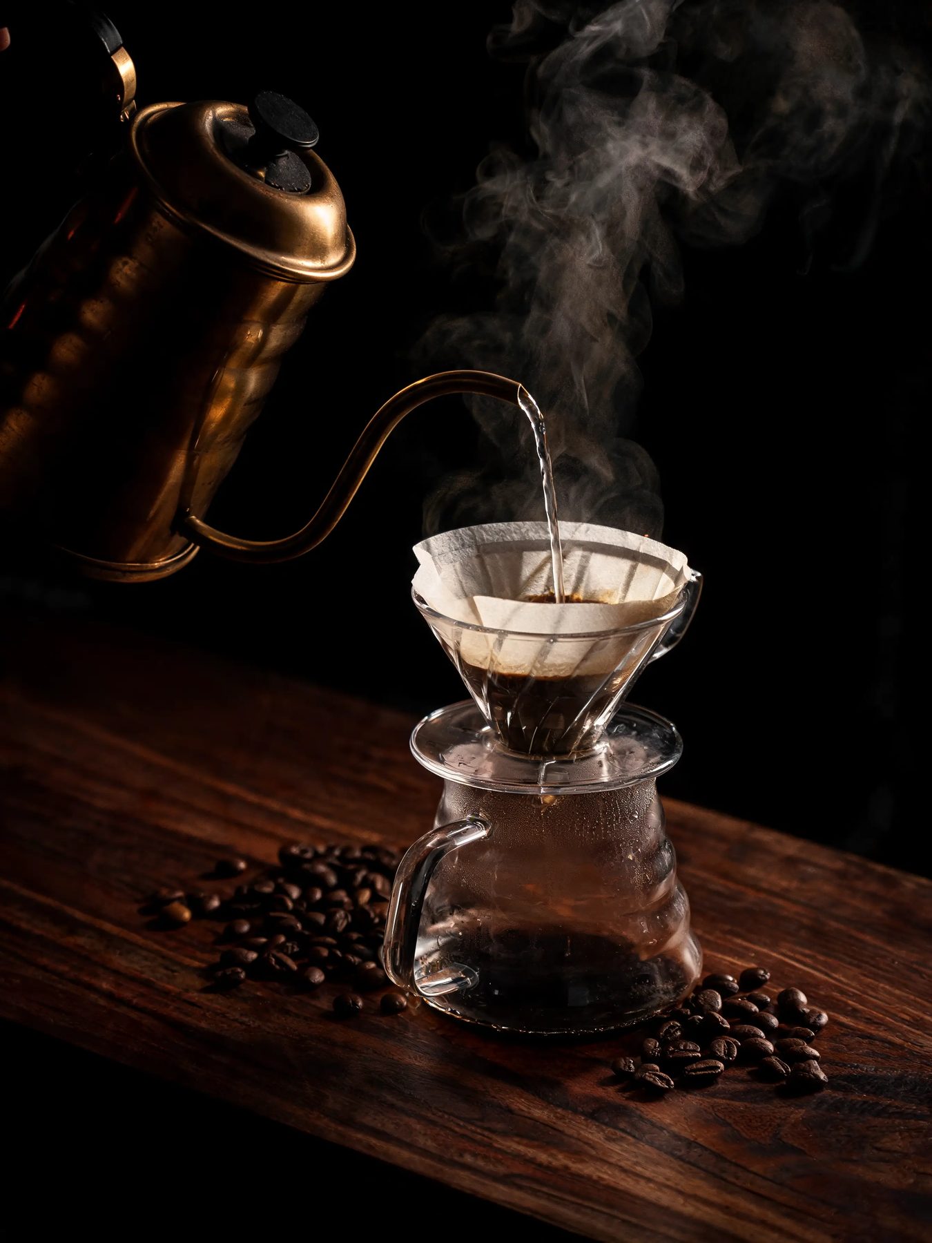 Gooseneck kettle pouring into a glass dripper on a dark walnut counter